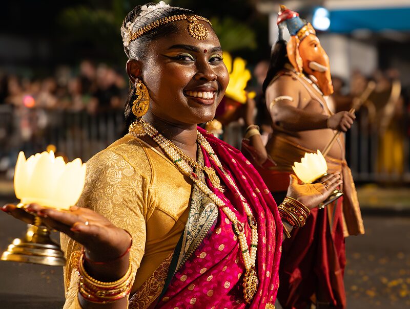 Jeune danseuse indienne souriante avec des fleurs illuminées dans chaque main, lors du défilé du Dipavali de Saint-André, Réunion.